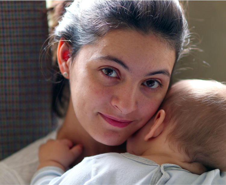 A mom looking at the camera while carrying her baby