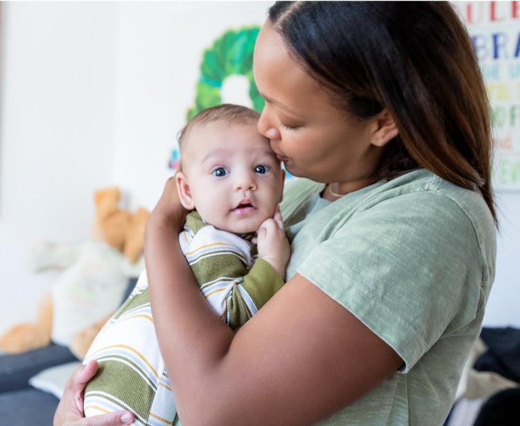 A women with brown hair, in a green tshirt, hugging and kissing her baby