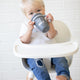 Sip Sip Hooray Happy Sippy Cup by Bella Tunno being held by a kid while in a high chair