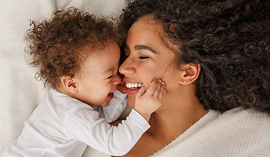 A mom and her baby laughing together on the bed