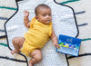 Newborn Essentials Gift Set beside a Baby lying down in yellow onesie